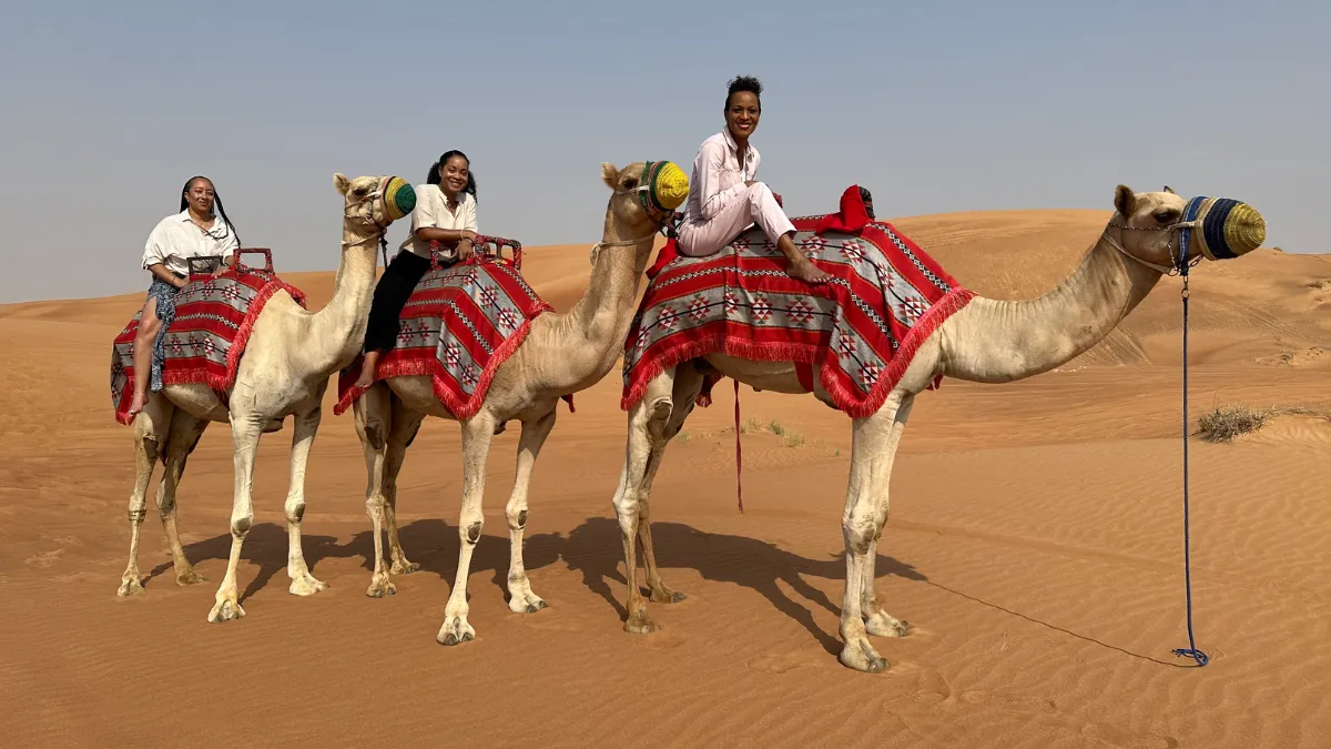 Three travelers riding camels across desert dunes