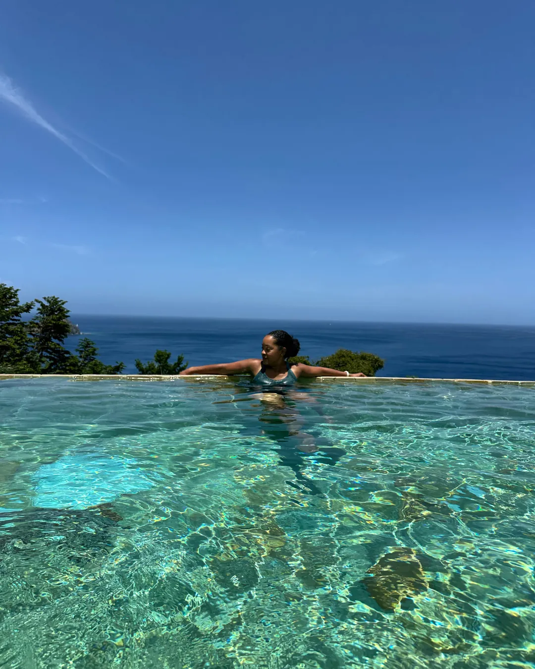 A guest floating at the edge of an infinity pool above the Caribbean Sea