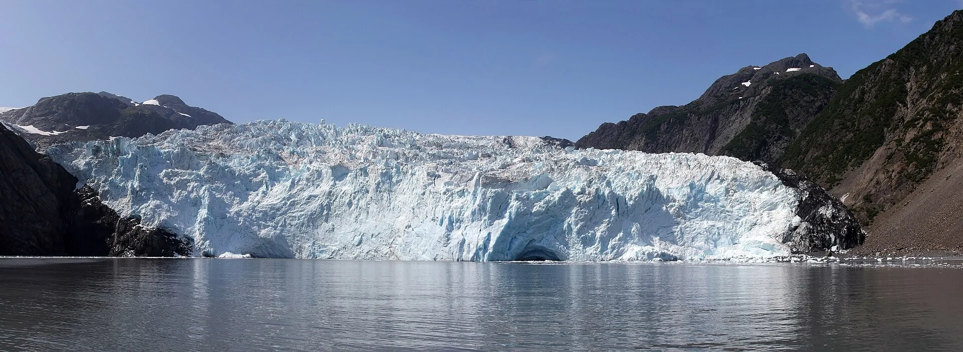 A tidewater glacier meeting the sea beneath snow-capped mountains in Alaska