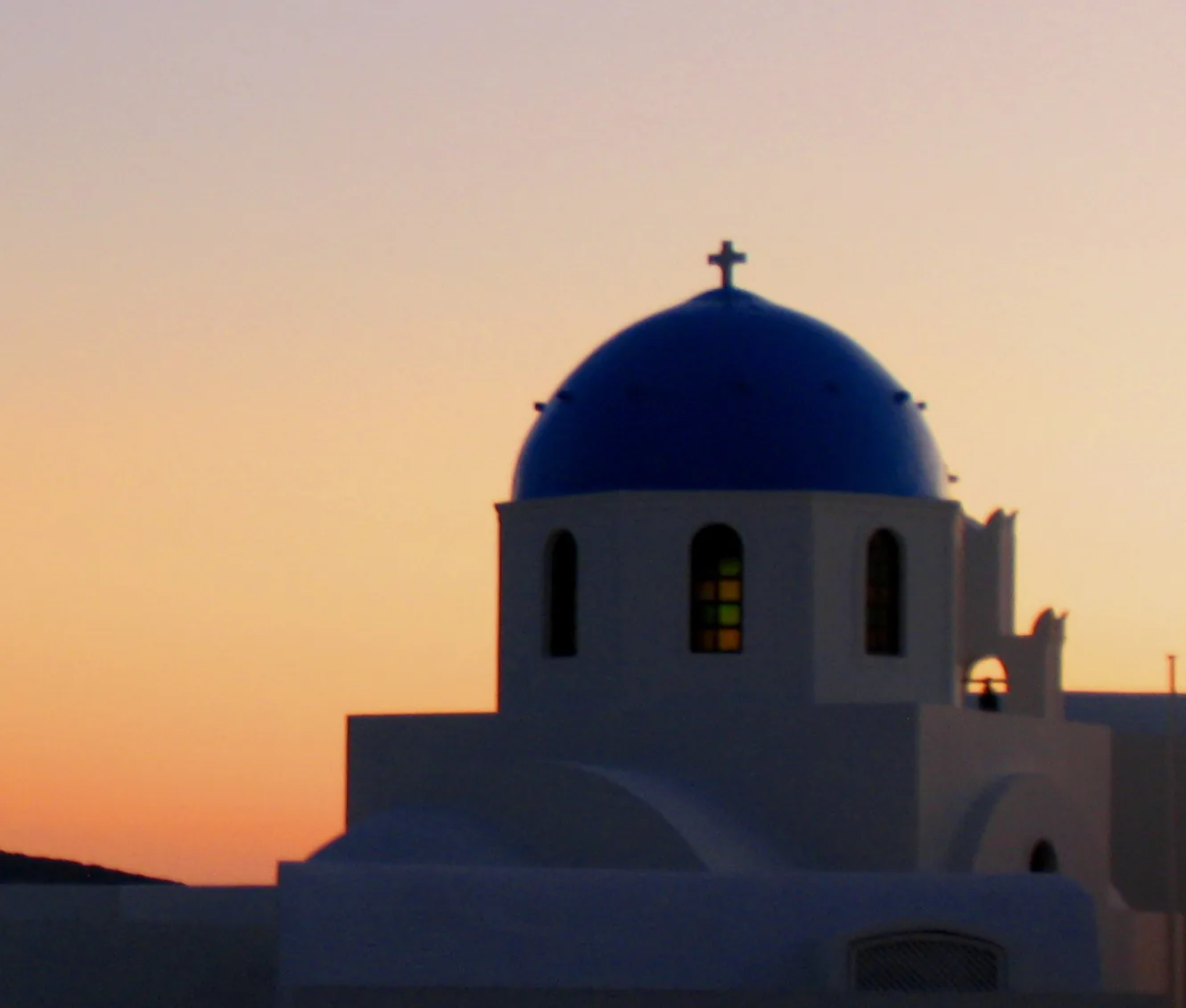 A blue-domed white church in Oia, Santorini, glowing against a peach and orange sunset