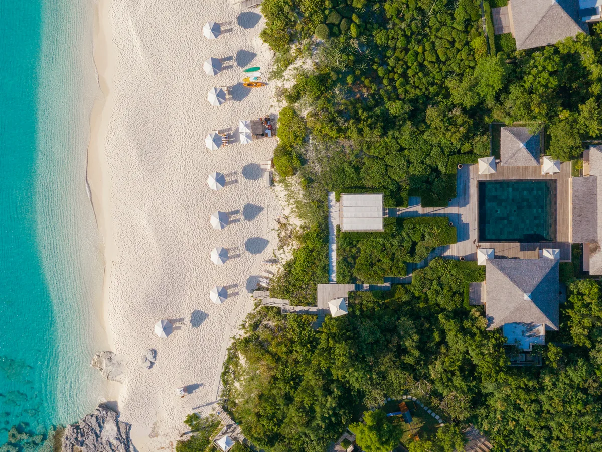 An intimate beachfront villa resort from above, pools and umbrellas tucked into tropical greenery