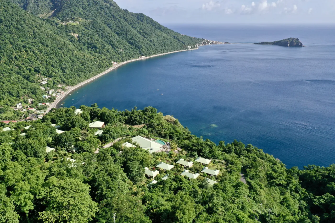 Villas tucked into a green hillside above a wide Caribbean bay