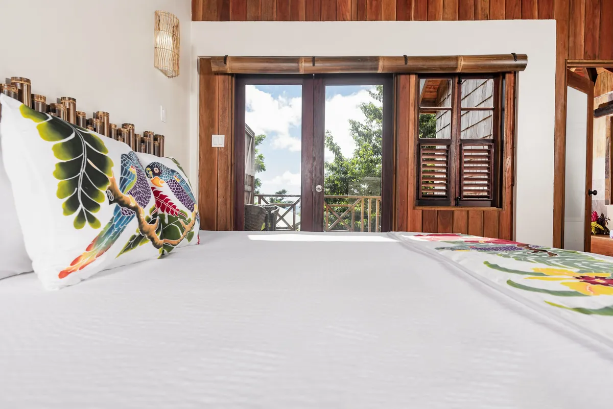 A bright suite with a king bed, hand-painted pillows, and doors opening to a private terrace
